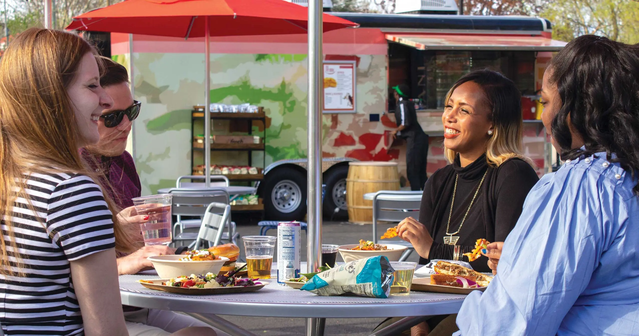 4 individuals eating at a table with food truck in backdrop