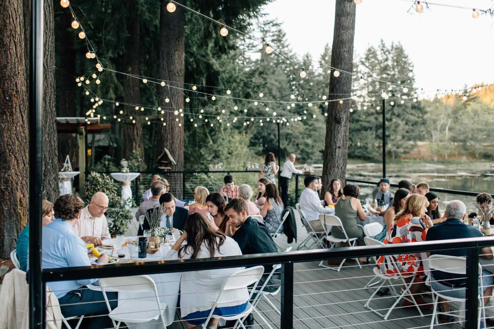 Guest eating at outdoor tables with view of woods and water in the background