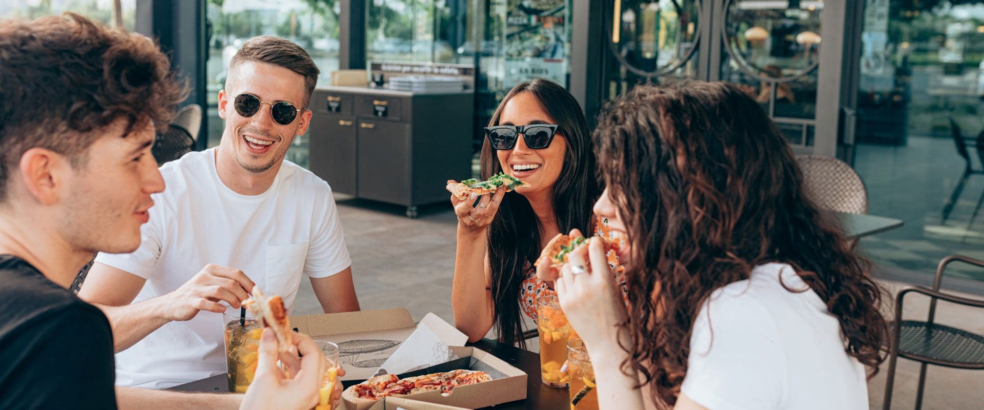 Young individuals eating pizza outside restaurant