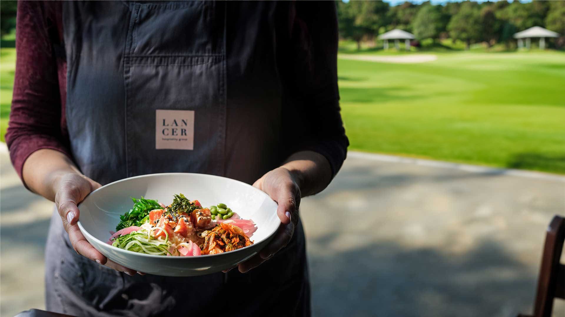 Server holding dish in front of golf course