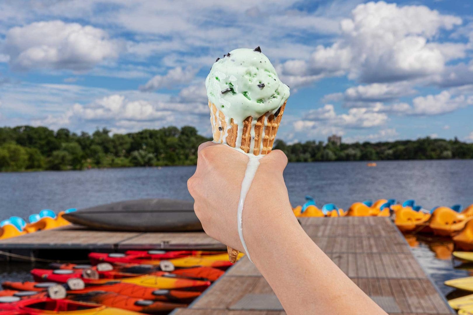 Hand holding ice cream cone that is melting, sky and lake in the background